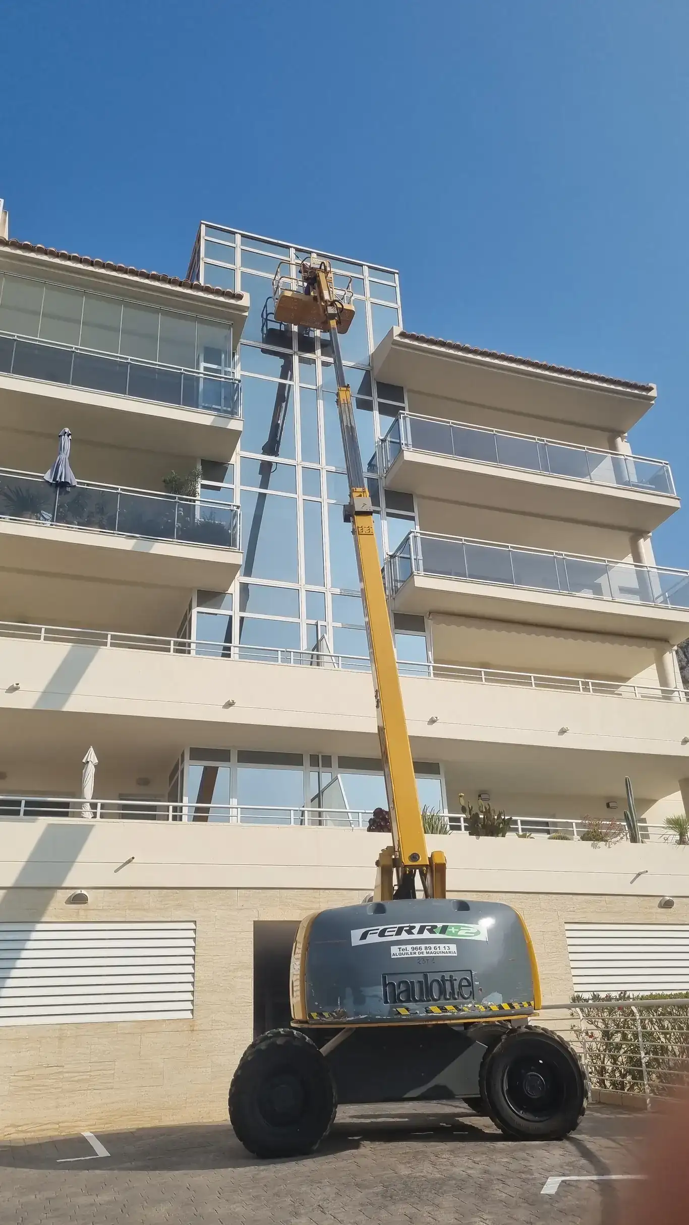 Servicio de limpieza de cristales de fachada principal de hotel mediante grúa elevadora.