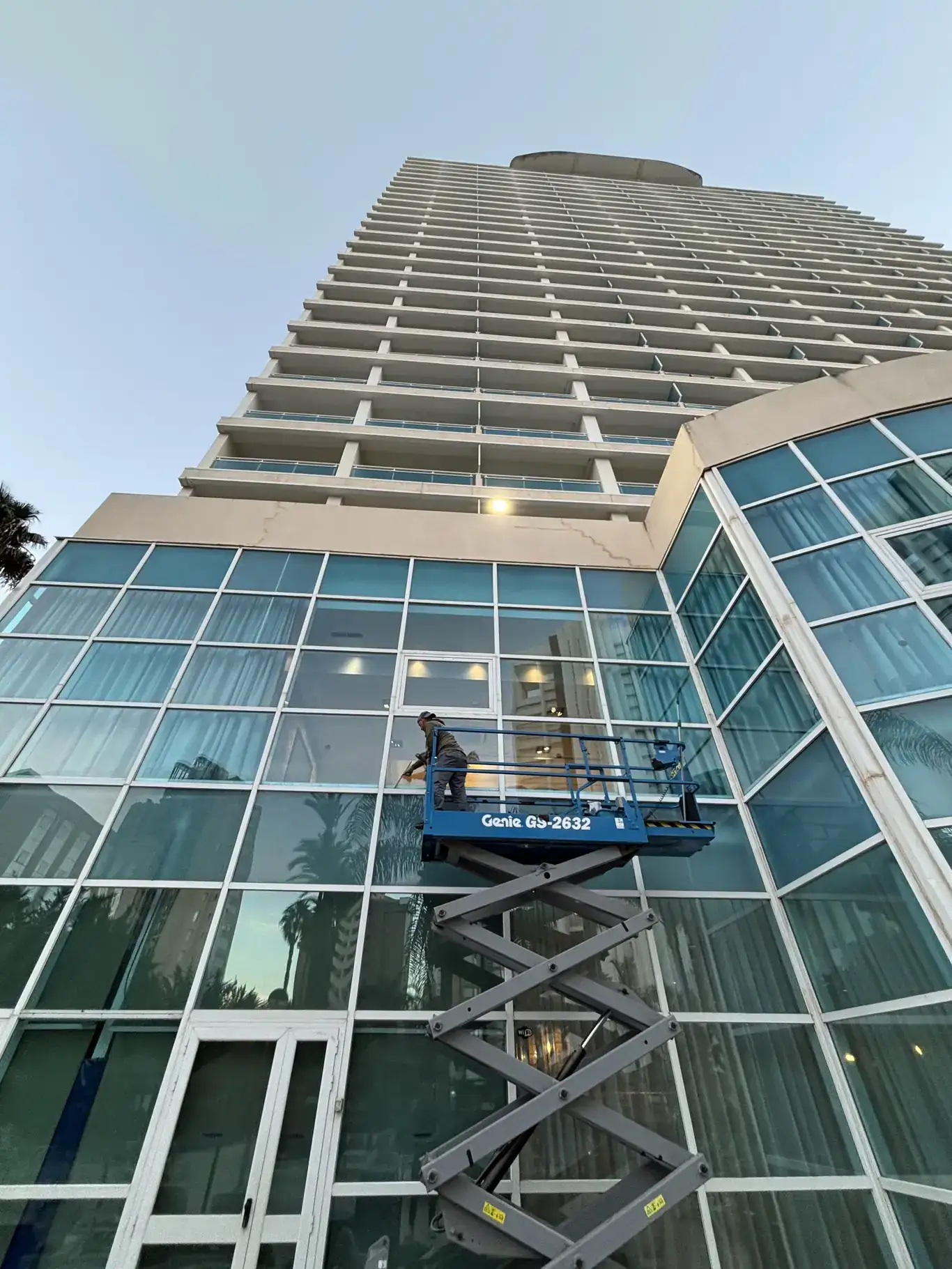 Operario realizando limpieza de fachada de cristal con plataforma de tijera en gran edificio.