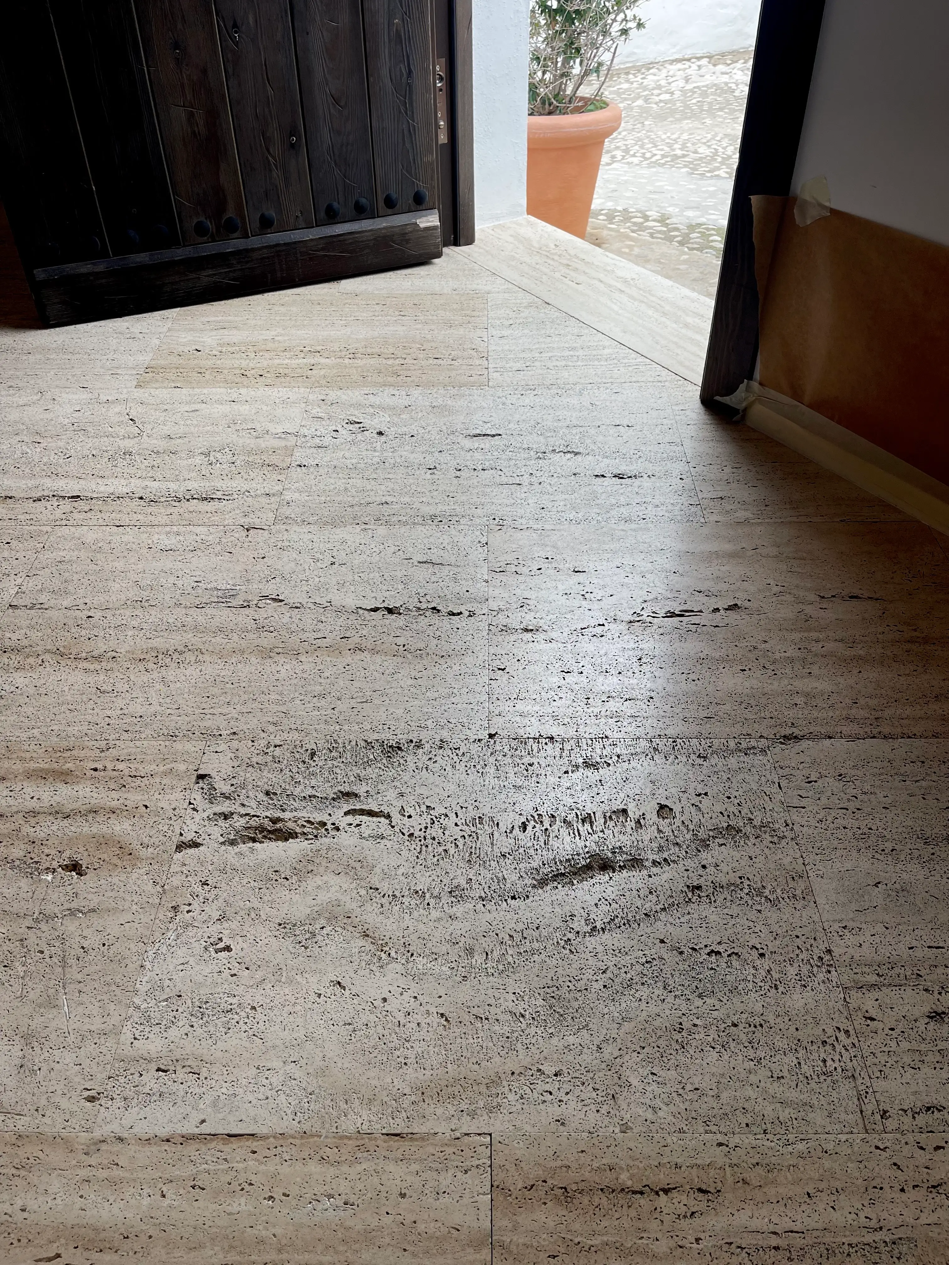 Deteriorated travertine marble floor with open joints and stains before restoration in Altea